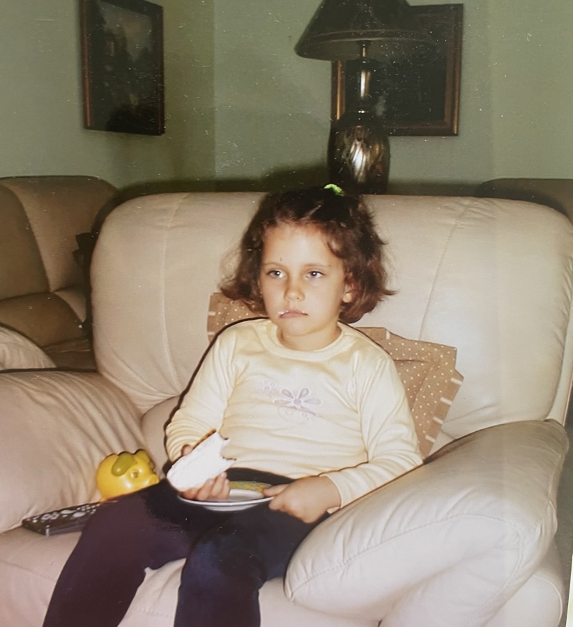 Natalia as a kid on the couch with a snack
